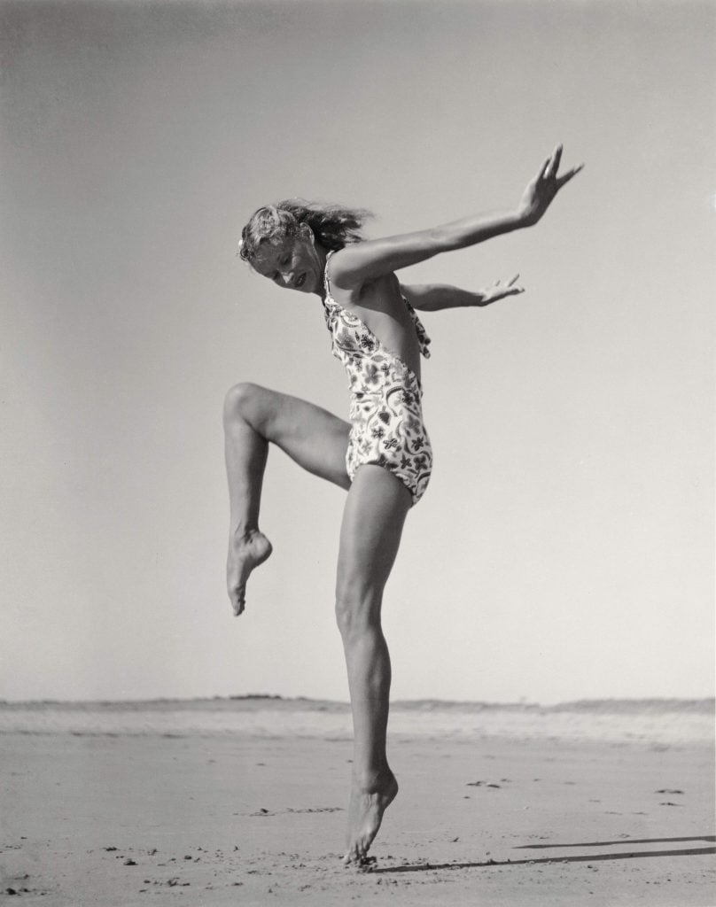 a black and white profile shot of supermodel Lisa Fonssagrives jumping at the beach, striking a dance pose