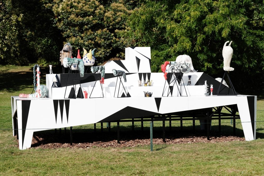 a large white structure like a table but with shelves, a display on which is perched various small sculptures that appear to be fantastical reimaginings of human body parts