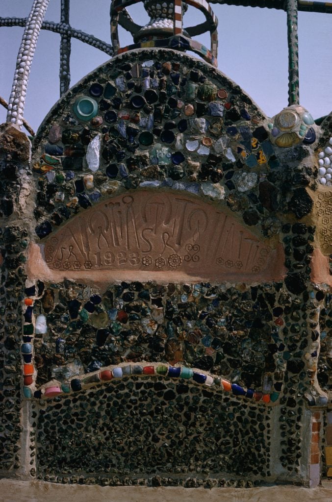 at archway at the entrance to the Watts Towers consists of a mosaic of glass and otehr found objects, including the artists intials "SR" imprinted into the concrete