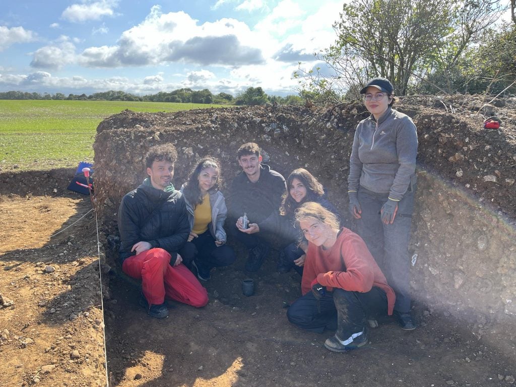 a group of stuents huddle in front of a low wall, one holds up a vial