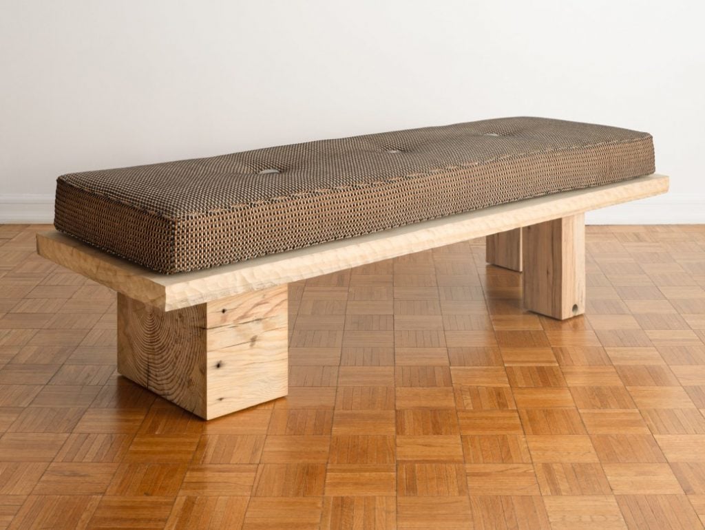 an austere bench is made of wood with a brown cushion atop 