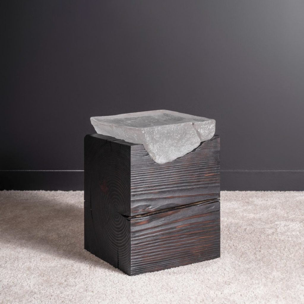 a side table has a stone gemlike glass top on top of a dark wood base it sits atop white carpet 