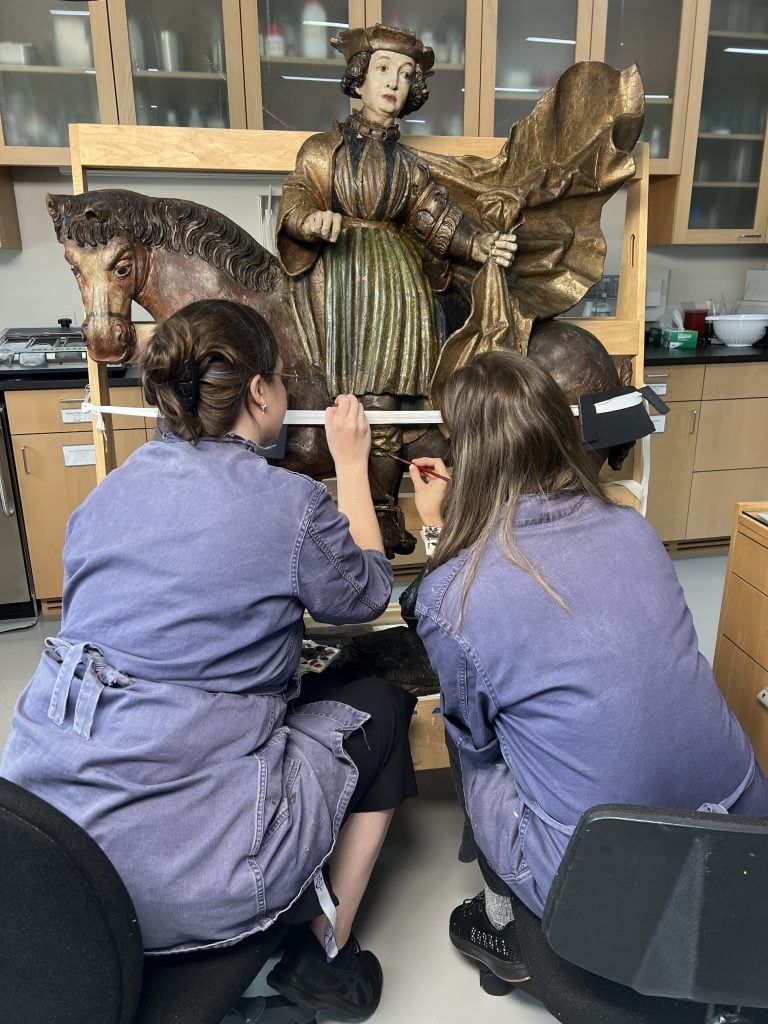 Two women work on restoring a sculpture