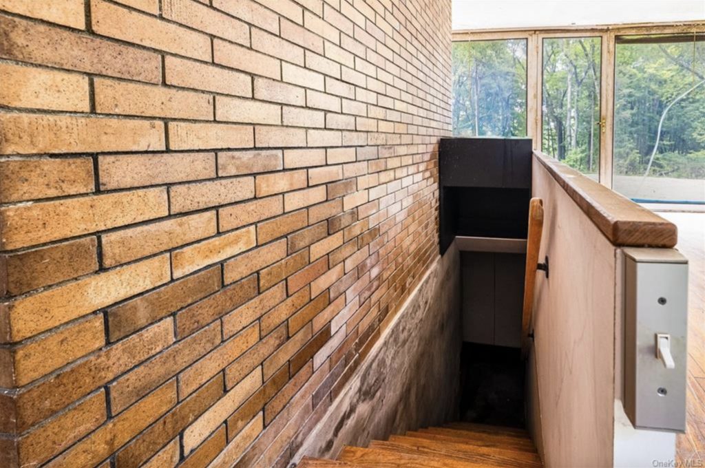 A photograph of the empty Booth House, looking down a stairwell set against a brick wall from atop it.