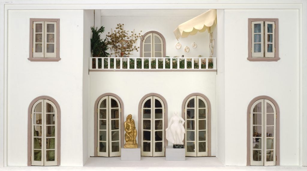 Dollhouse courtyard with statues and a balcony lined with plants.