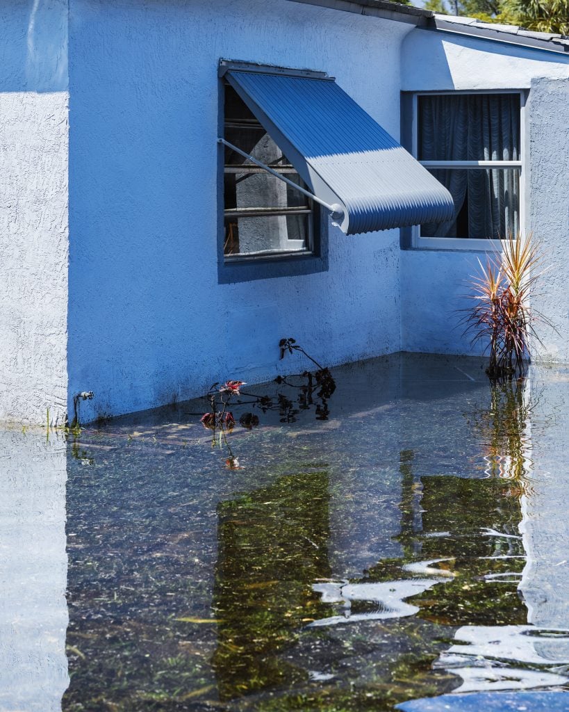 a blue cement house with a blue awning, with water high in front of the house