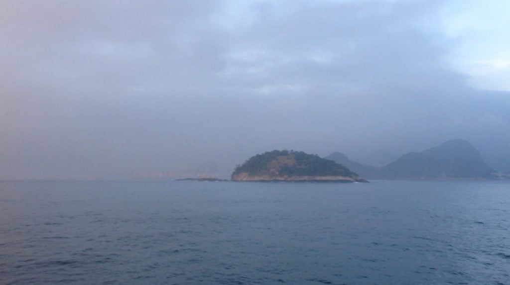 A small island in the Atlantic Ocean seen in front of an atmospheric cloudy sky.