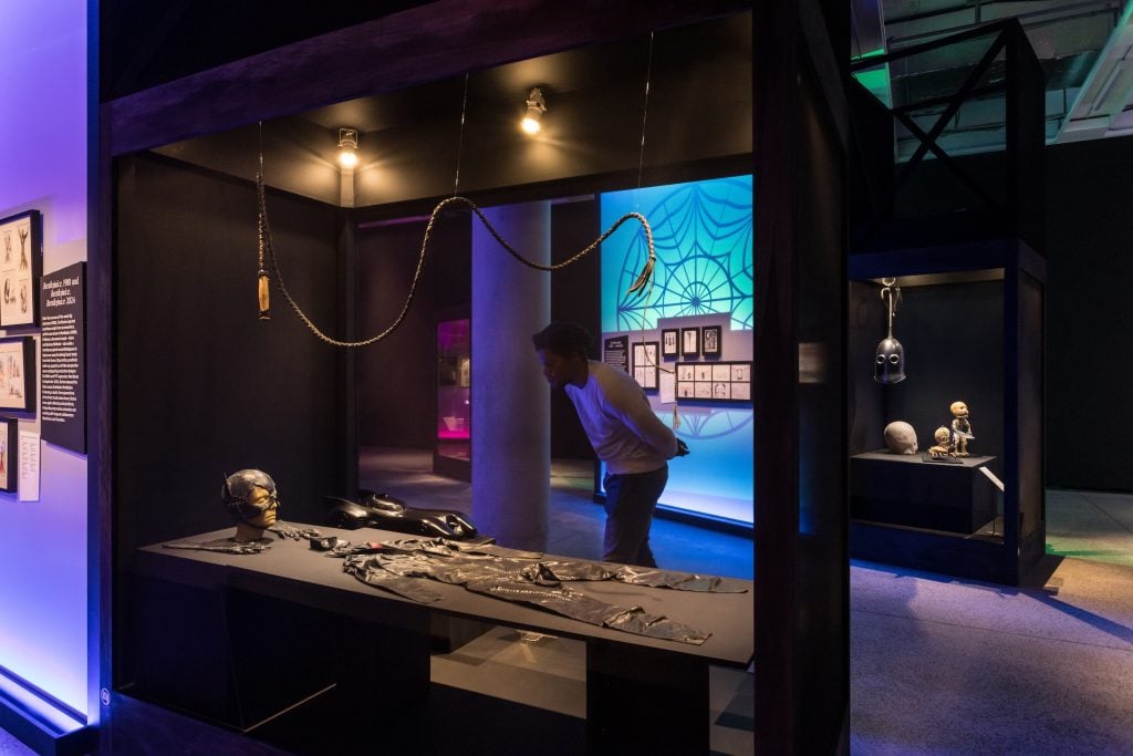 A person looking at Catwoman suit at Tim Burton exhibition, against a blue-lit backdrop