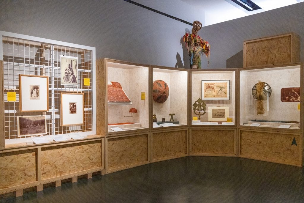  A museum exhibit displaying cultural artifacts, historical photographs, and traditional art pieces in wooden-framed glass cases.