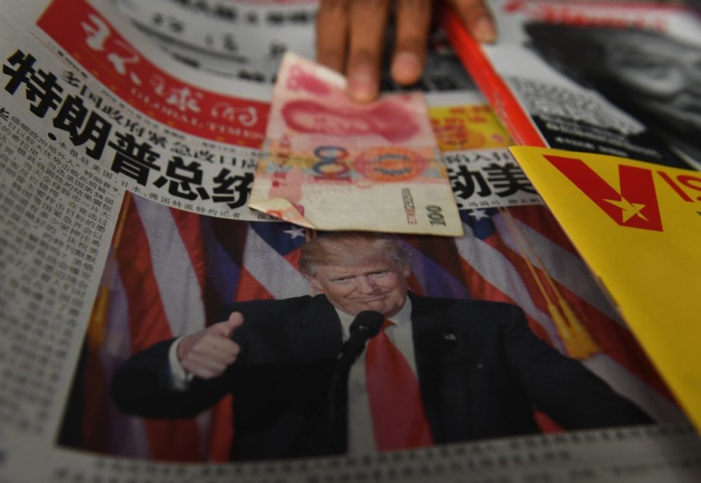 A hand holds Chinese currency atop a newspaper with Donald Trump on the front page