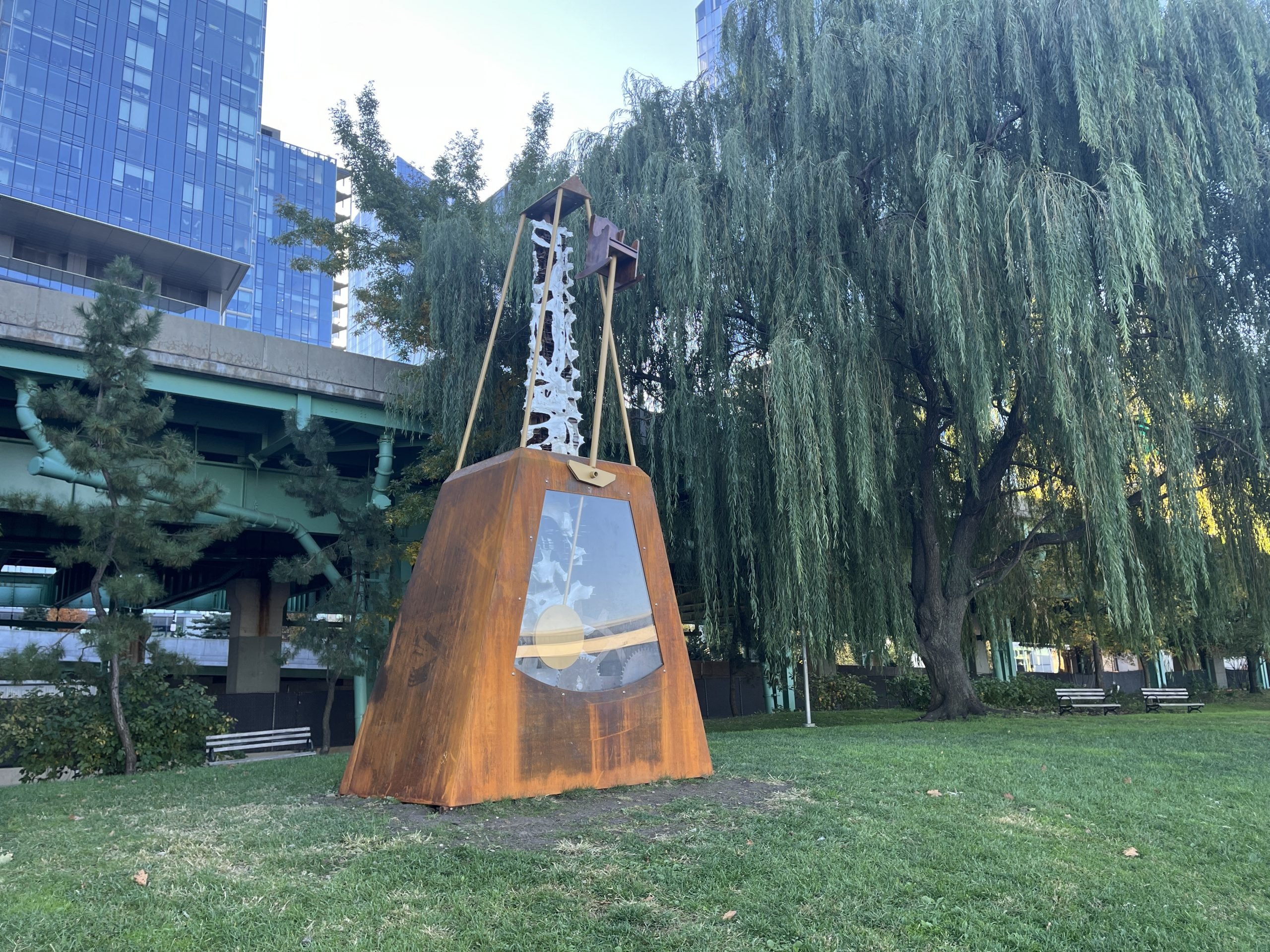 A giant metronome sits in a park beneath a highway