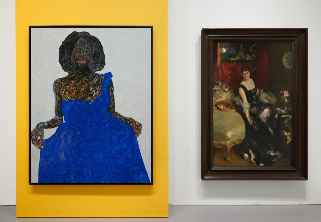 an interior of amuseum with two portraits hanging side by side, on the left is a Black woman wearing a colbalt blue dress and on the right is a traditional portrait of a white women seated in an opulent interior in a black dress