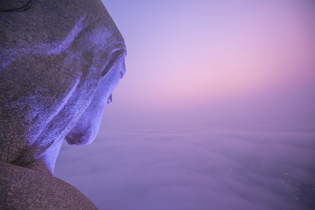 Isaac "Driftershoots" Wright's photograph atop Christ the Redeemer in Brazil. The head of the statue is seen from a camera somewhere on the arm, looking off into the haze of a purple sunrise.