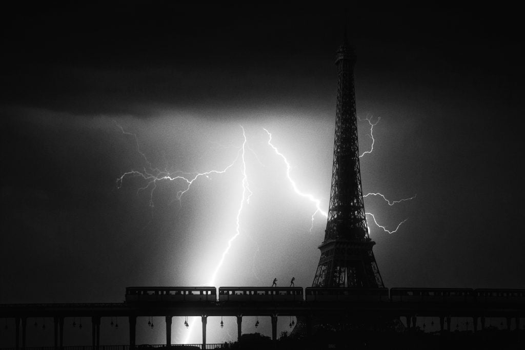 Isaac "Driftershoots" Wright's photograph of the Eiffel Tower. The black and white image is taken at night, the tower dramatically silhouetted by a giant bolt of lightning behind it. 