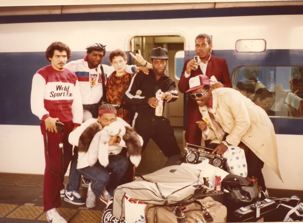 a 1970s photo of a group of men and one woman. The men are mostly wearing maroon and white track suits