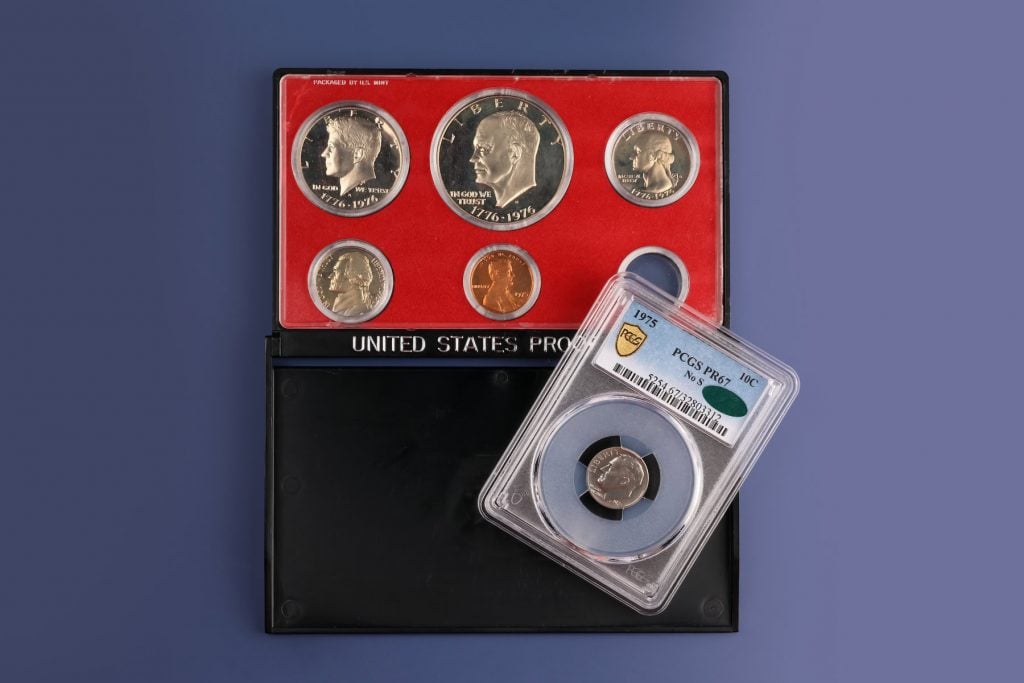 a silver coin with an engraving of an old man inside a plastic display case on top of a larger red display case containing other silver and gold coins with images of old men on them