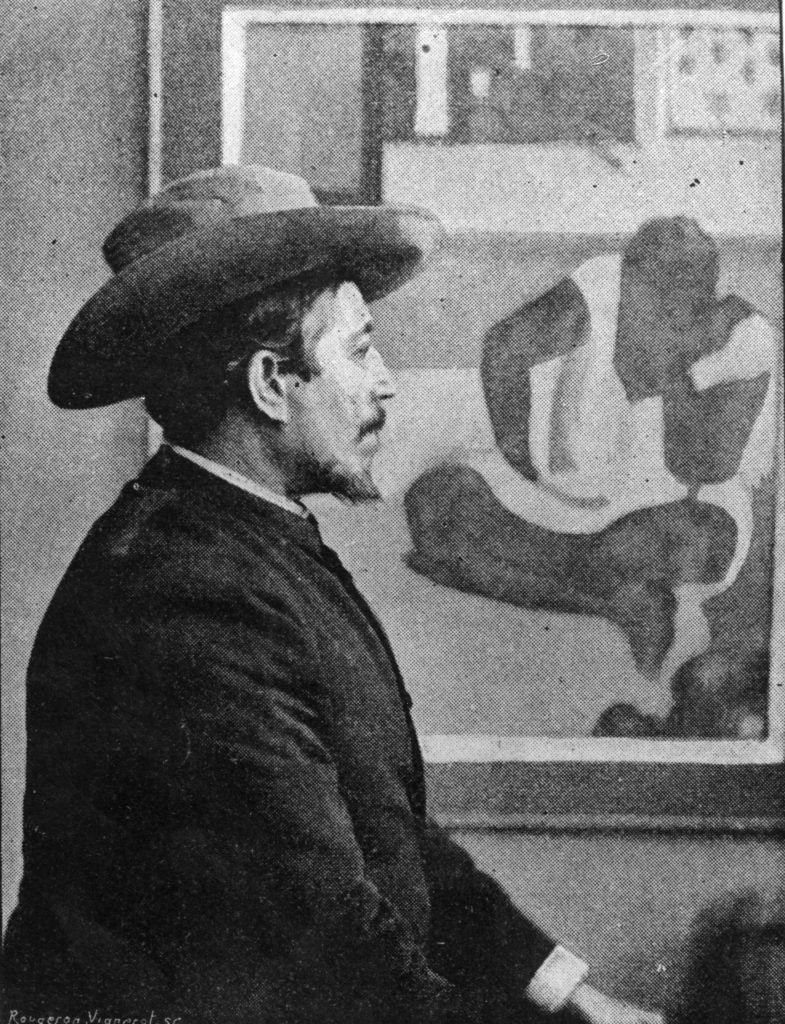 Paul Gauguin in a hat sitting in profile in front one of his paintings