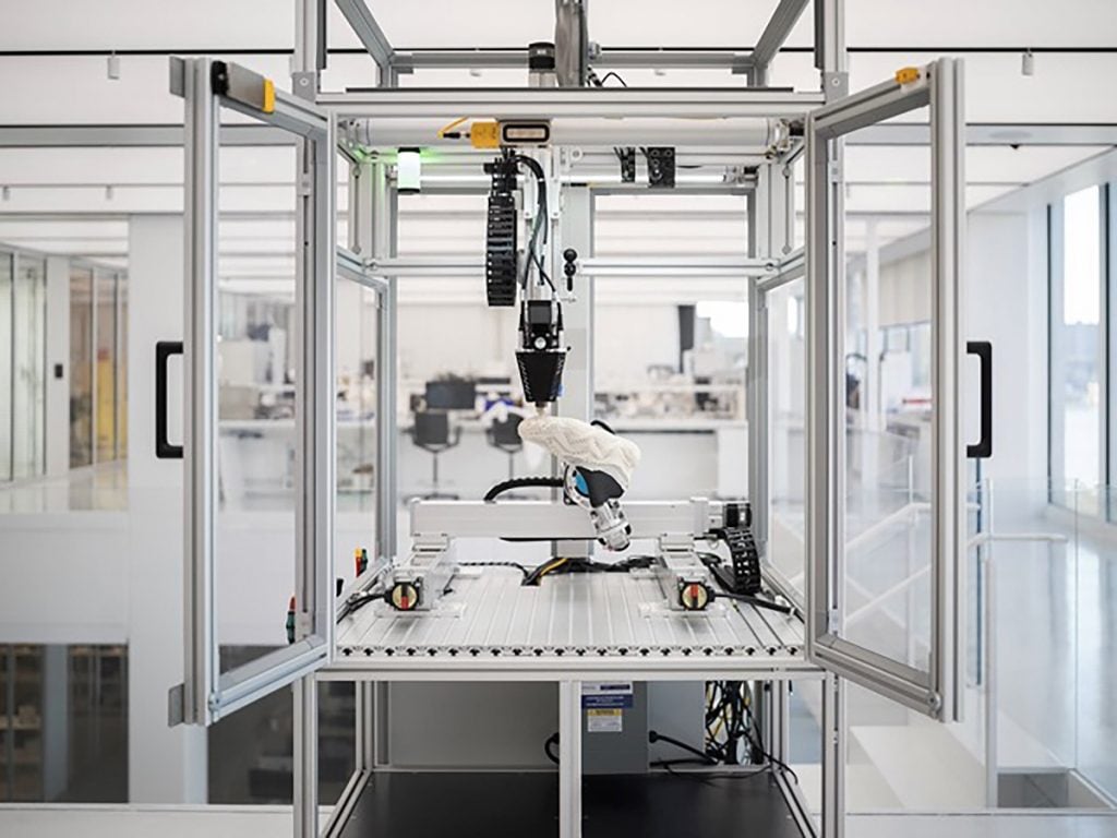 A five-axis, 3D printer in a glass case printing a shoe