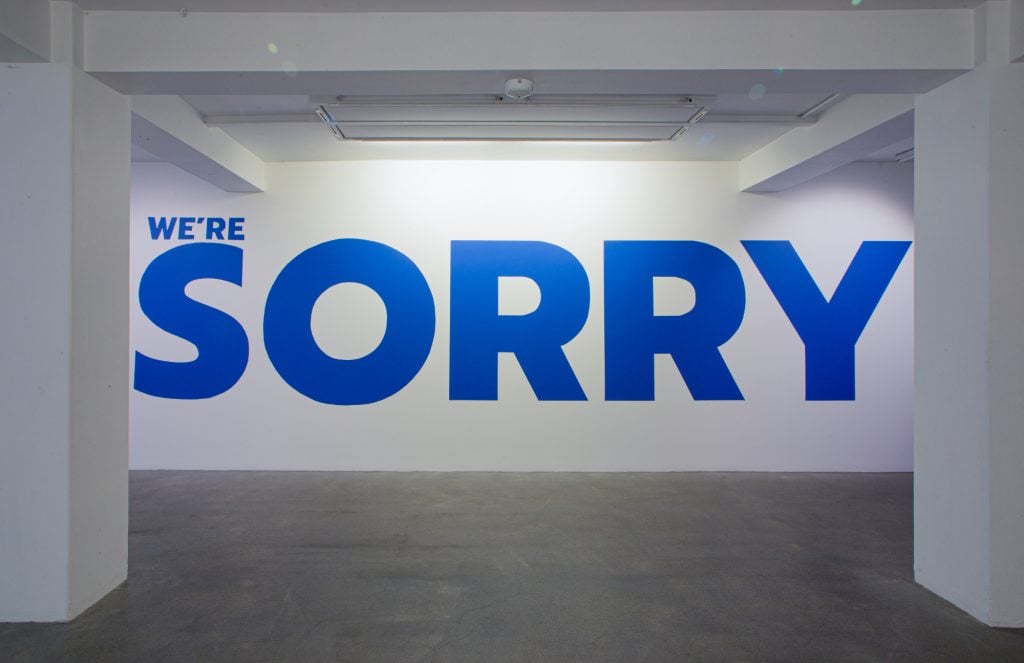 a white wall with the words 'we're sorry' written on it in big blue font