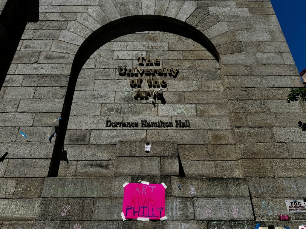 A grey brick wall with the letters "The University of the Arts" hung with protest signs