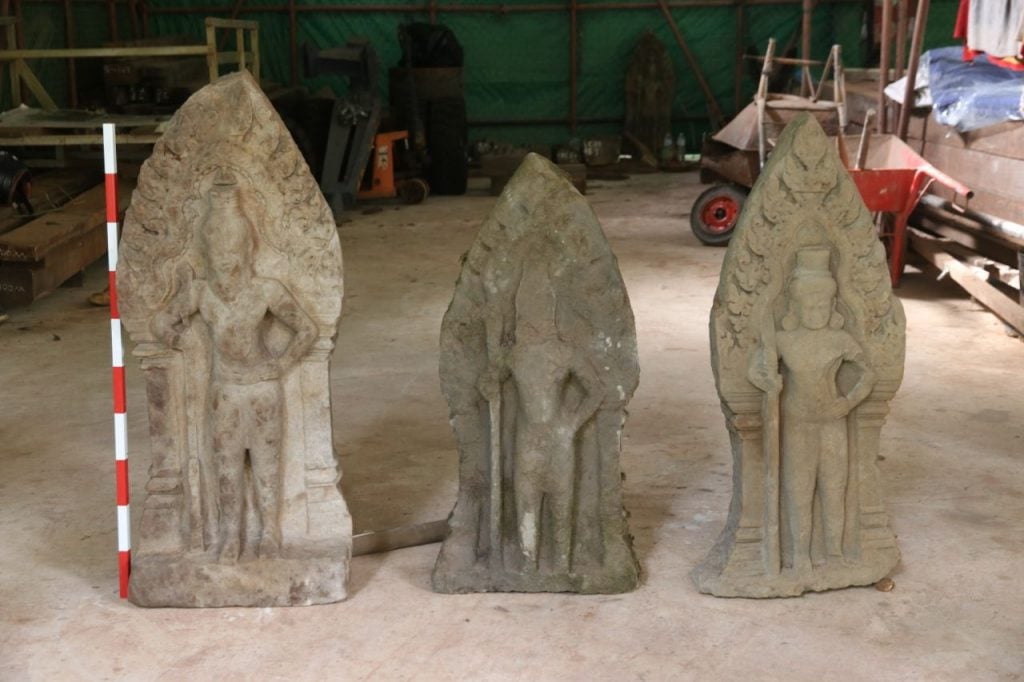 three small statues side by side on a dirt ground