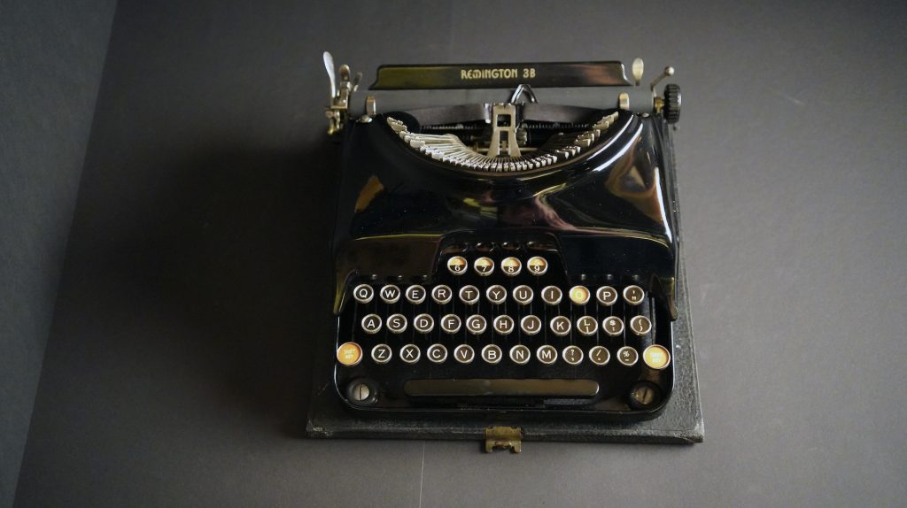 A photograph taken from above of a vintage black typewriter, on a grey background.