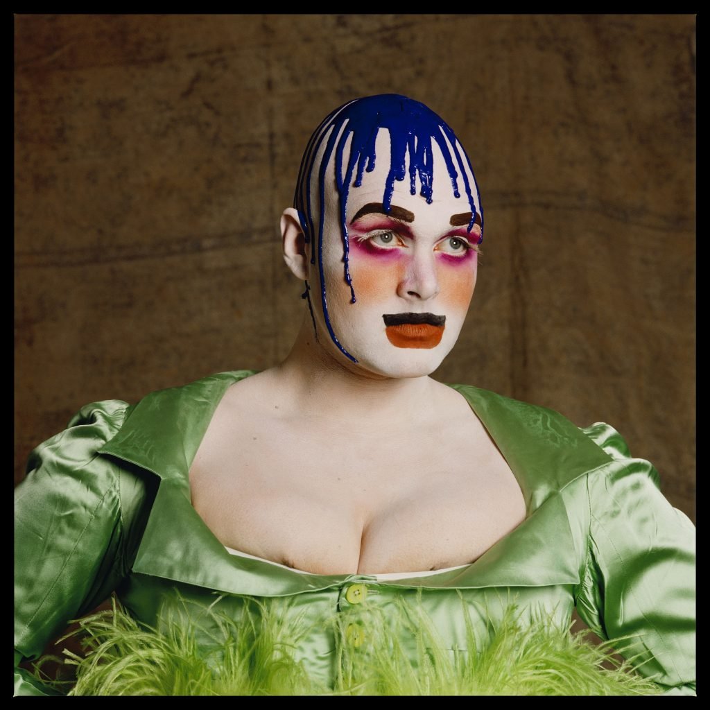 a portrait of Leigh Bowery in drag makeup and purple paint dripped on their head. 