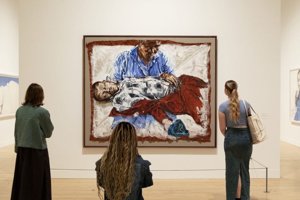 three people look at a large painting depicting two people in an art gallery