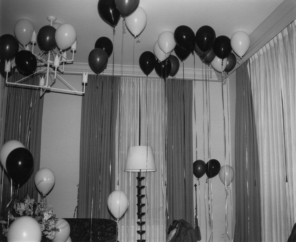 Black and white balloons float against tall curtains in a room, anchored by thin ribbons.