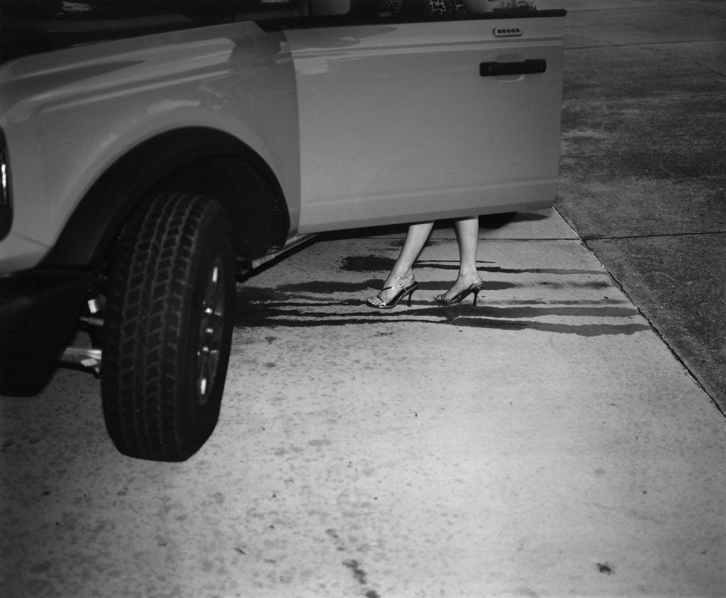 Woman’s legs in heels step out of a car, leaving water streaks on the pavement.