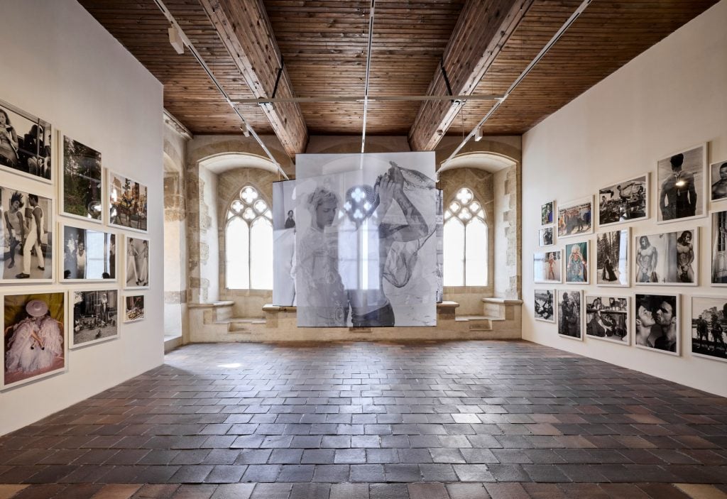 A photography exhibition in a historic hall with framed images and layered translucent hanging photographs.