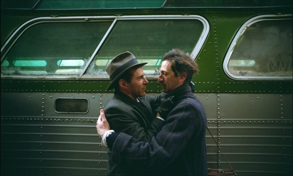 Actors Adrien Brody and Alessandro Nivola embrace next to a vintage bus in the movie The Brutalist