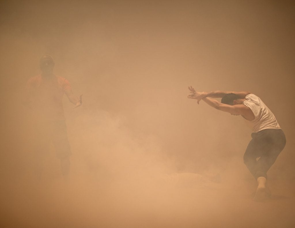 A photograph of two dancers faintly visible through a sepia-tinged cloud.