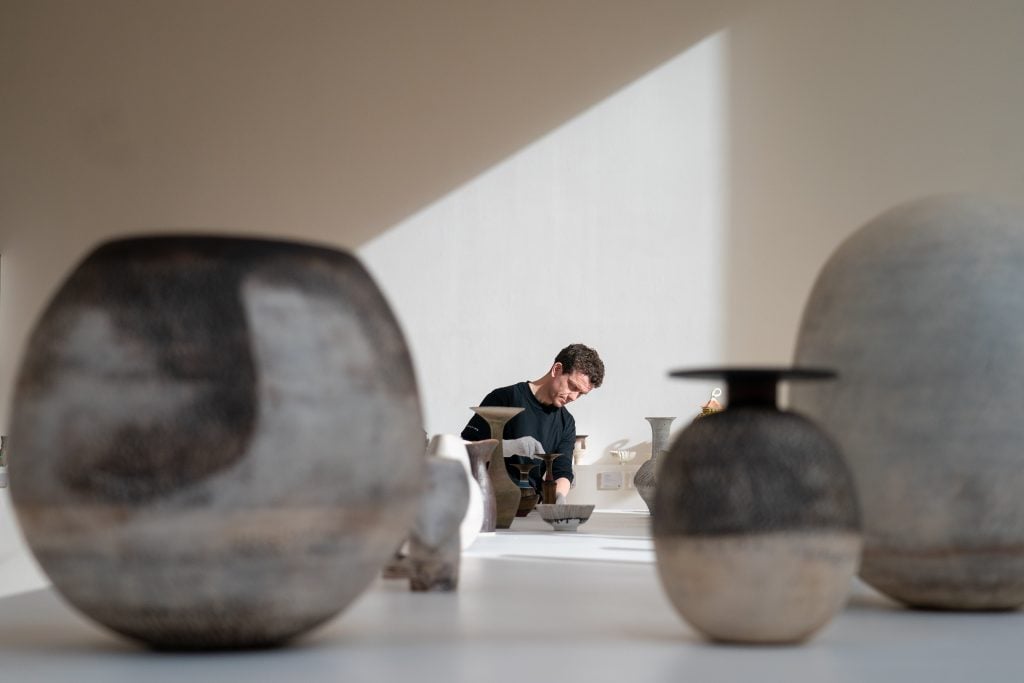 A man arranging a table of ceramics by Lucie Rie