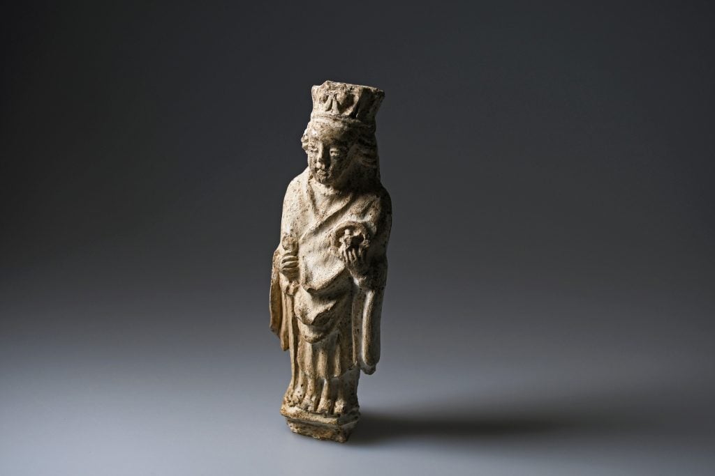 A photograph depicting the small white statue of Saint Catherine found beneath Molkenmarkt standing on a shaded gray background.