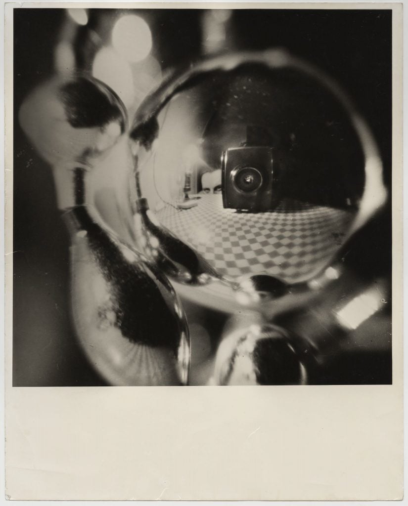 A black and white Surrealist self portrait taken in the surface of a curved, reflective metal object to give it a fish eye distortion.