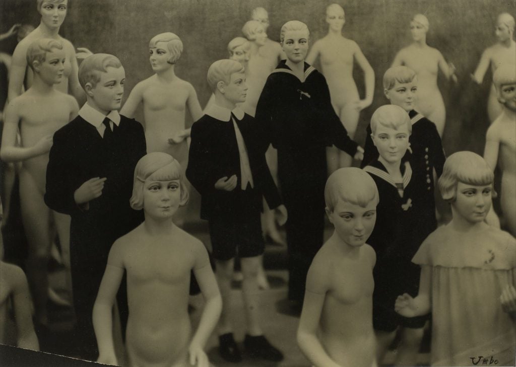 A yellow-tinged surrealist photograph depicting a crowd of young male mannequins, some clothed and some not.